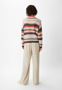 Sweter w paski z delikatnych pastelowych kolorów, z różnorodnymi poziomymi paskami. W zestawie z jasnobeżowymi spodniami o szerokich nogawkach i sportowymi sneakersami.