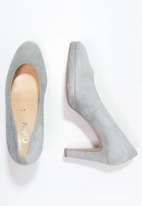 Chaussures à talons hauts en daim gris avec un bout rond, présentant une texture lisse et un talon carré de 7 cm. Marque visible sur la semelle intérieure.