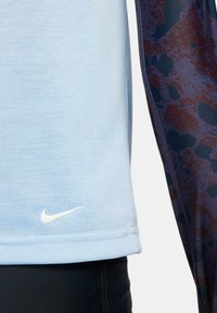 Camiseta atlética azul claro con una textura suave, que presenta un pequeño logo blanco de Nike y un acento oscuro con patrón a lo largo del costado.