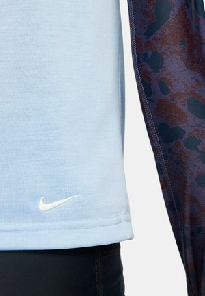 Jasnoniebieska koszulka sportowa o gładkiej fakturze, z małym białym logo Nike i ciemnym wzorem wzdłuż boku.