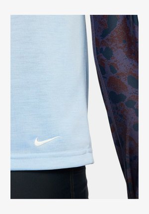 Jasnoniebieska koszulka sportowa o gładkiej fakturze, z małym białym logo Nike i ciemnym wzorem wzdłuż boku.