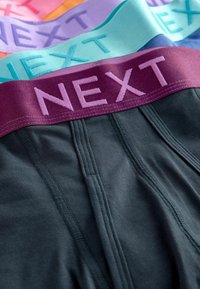 Sötét szürke boxeralsó, puha elasztikus derékkal, amelyen világos rózsaszín "NEXT" felirat található. Pasztell színű sávokkal kiegészítve narancssárga, lila és türkiz árnyalatban.