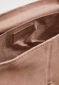 Měkká růžová tkaninová taška uvnitř s hladkou texturou, s označením "KIOMI" raženým na nálepce. Viditelné švy podél okrajů.