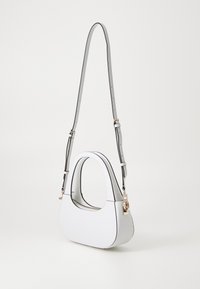 Borsa in similpelle bianca con forma curva, tracolla grigia regolabile e dettagli dorati. Presenta una texture sottile e una finitura a contrasto.