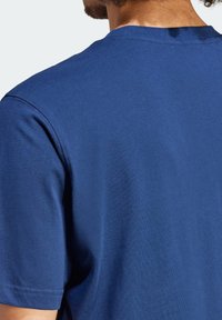 Modré bavlněné tričko s kulatým výstřihem, krátkými rukávy a hladkou strukturou. Viditelné švy podél ramen a rukávů.