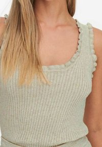 Camiseta sin mangas verde claro con bordes ondulados, hecha de textura suave. El escote es redondeado y las tirantes se ajustan planas sobre los hombros.