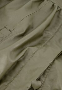 Olijfgroene zachte leren kleding detail met hartvormige knoop en subtiele stiksels.