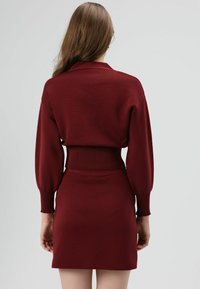 Ensemble bordeaux deux pièces composé d'un haut en tricot avec col et manches ballon, associé à une jupe ajustée assortie. Texture lisse.