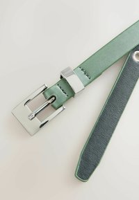 Grøn læderbælte med en glat overflade, et sølvfarvet rektangulært spænde og let kontrasterende syninger. Kanterne er afsluttet i en mørkere grøn farve.