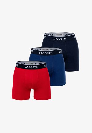 Drie paar Lacoste boxershorts in rood, marineblauw en donkerblauw. Elk met een merk-elastische tailleband en een aansluitend ontwerp.