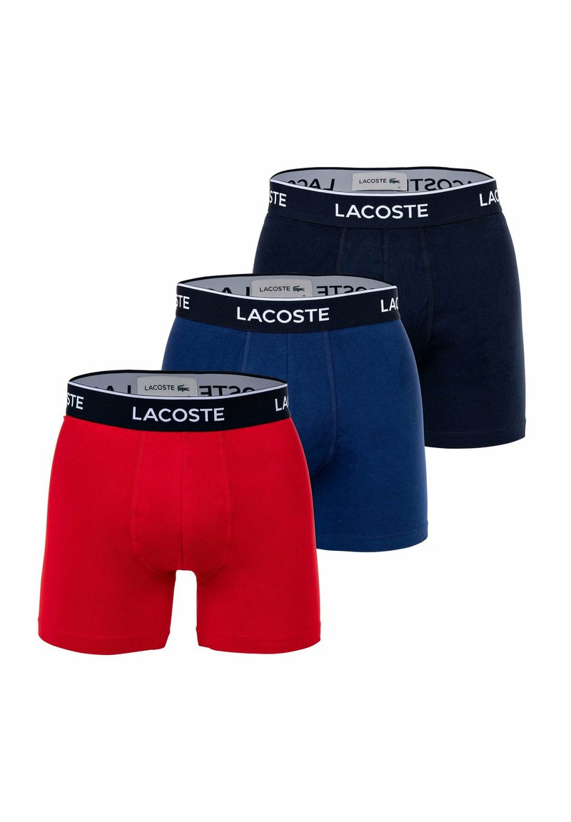 Három pár Lacoste boxer alsónadrág piros, sötétkék és sötétkék színben. Mindegyik márkázott, rugalmas derékpánttal és testhezálló dizájnnal rendelkezik.
