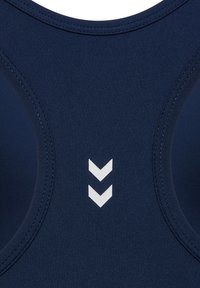 Close-up van marineblauwe sportstof met twee witte, naar beneden wijzende chevrons dicht bij de middennaad gestikt.