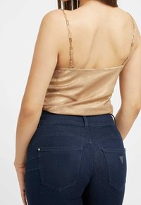 Zlatá metalická tílko s řetízkovými ramínky, v kombinaci s tmavě modrými slim kalhotami s zadními kapsami a jemnými švy.