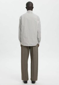 Črtasta srajca v svetlo bež in rjavi barvi, izdelana iz tkanine z gladko teksturo, v kombinaciji s širokimi bež hlačami.