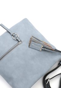 Borsa in finta pelle blu chiaro con una texture liscia, dotata di una cerniera argentata, un tassello decorativo e una tracolla regolabile. Brand visibile.