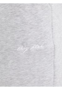 Šviesiai pilka medžiaga su subtiliu balto siuvinėto kursyvo tekstu prie siūlės, rodanti tekstūros ir siuvinėjimo detales.