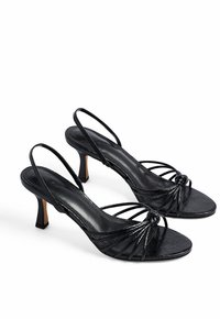 Tacchi neri con cinturini, superficie testurizzata, tacco sottile e dettaglio annodato sulla punta. Presentano cinturini slingback regolabili.