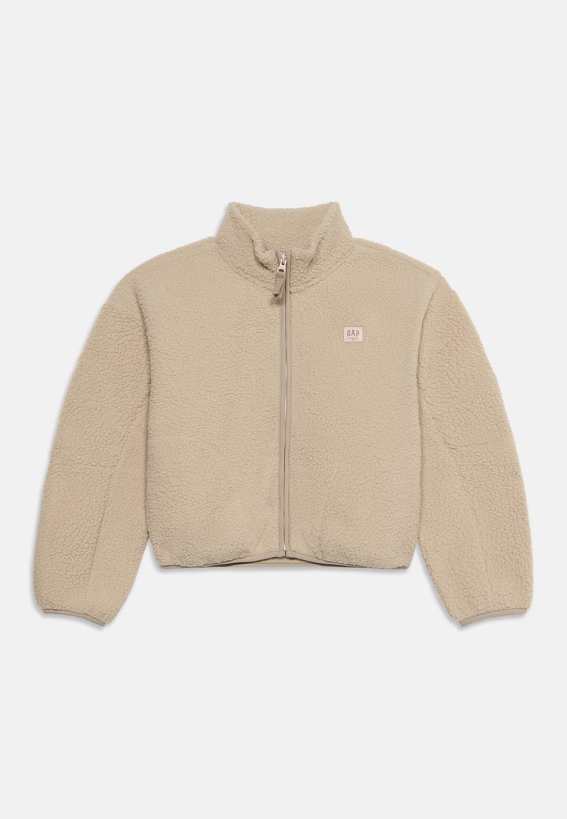 Veste polaire beige à fermeture éclair, duveteuse, manches longues, avec un petit patch logo rectangulaire sur la poitrine gauche.