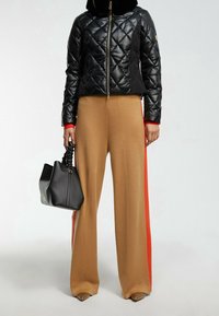 Svart kviltad pufferjacka med dragkedja, röda manschetter; beige vida byxor med röda sidopaneler; svart läderhandväska med rynkad handtag.