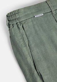 Pantalon en lin vert avec taille élastique, poche latérale et petite étiquette "MR MARVIS" sur le côté supérieur près de la boucle de ceinture.