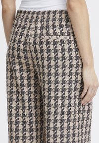 Houndstooth-musterte Hosen in Beige und Schwarz mit elastischem Bund und einer Gesäßtasche. Strukturierter Stoff mit weicher Oberfläche.