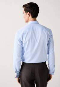 Chemise bleu clair à manches longues avec un motif subtil, poignets boutonnés comportant des accents de couleur contrastante, associée à un pantalon rayé sombre.