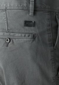 Sive hlače iz jeansa z malo črno oznako "JOOP! JEANS". Ena zadnja žep z gumbnim zapiranjem. Gladka, mehka tekstura.