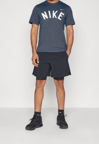 Miestenské námornícke tričko Nike s bielym logom, doplnené čiernymi šortkami. Obsahuje ľahký materiál a atletický strih pre pohodlie a pohyblivosť.