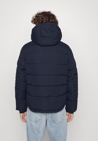 Marinblå puffjacka med huva, med horisontella quiltade sektioner, elastiska ärmslut och avslappnad passform. Bakvy visar en slät yta.
