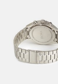 Hõbedane roostevabast terasest kell linkkellaga, kronograafi funktsioonide ja sujuva, ümmarguse korpusega. Tagaküljel on brändi nimi ja veekindluse näidud.