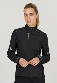 Schwarze Sportjacke mit hohem Kragen, Reißverschluss, reflektierenden Akzenten und elastischen Bündchen. Hergestellt aus leichtem, wasserabweisendem Material.