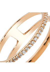 Bague en or rose présentant un anneau lisse et une rangée de petites pierres claires, avec un design géométrique ouvert et une finition polie.