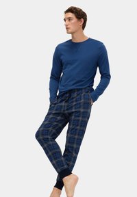 Blå langærmet skjorte parret med rutede pyjamasbukser i mørkeblå, sort og hvid, med snøre i livet og elastiske manchetter.