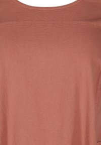 Texturerat tyg i en varm, dämpad terrakottafärg, med en rundad halsringning och draperad silhuett.