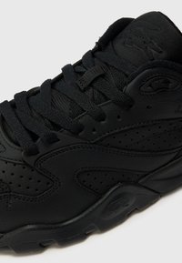 Black mid-top sneakers with a smooth leather upper, textured accents, perforations for breathability, and flat woven laces. Rubber outsole.
