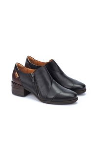 Bottines en cuir noir avec un bout pointu, fermeture éclair latérale et un petit talon empilé. Présentent un design entrecroisé et un intérieur marron.