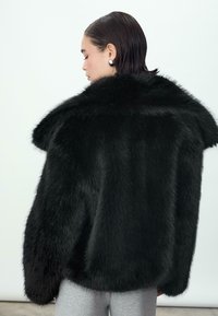 Giacca in pelliccia sintetica nera con ampio colletto e silhouette voluminosa. Presenta un materiale morbido e texturizzato e maniche lunghe e oversize.