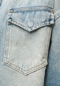 Τσέπη από ανοιχτό μπλε τζιν με καπάκι και πορτοκαλί ραφές σε φόντο ξεθωριασμένου τζιν υφάσματος.