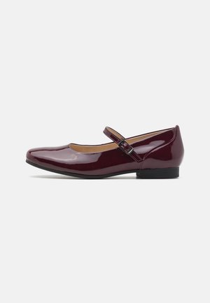 Chaussure Mary Jane en cuir verni bordeaux avec un bout arrondi, un talon plat et une sangle réglable. Texture lisse et design minimaliste.