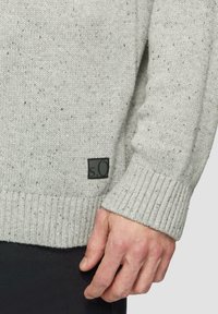 Jasnoszary sweter dziergany z teksturowym wzorem i ściągaczami na rękawach. Posiada małą czarną metkę z napisem "s.Oliver" z boku.