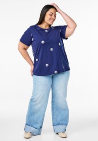 Námořnická modrá bavlněná tričko s krátkým rukávem, zdobené bílou květinovou výšivkou. V kombinaci s světle modrými volnými džínami.