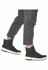 Bottines montantes noires en tissu texturé, avec semelles en caoutchouc blanc, fermeture éclair et col rembourré pour plus de confort.
