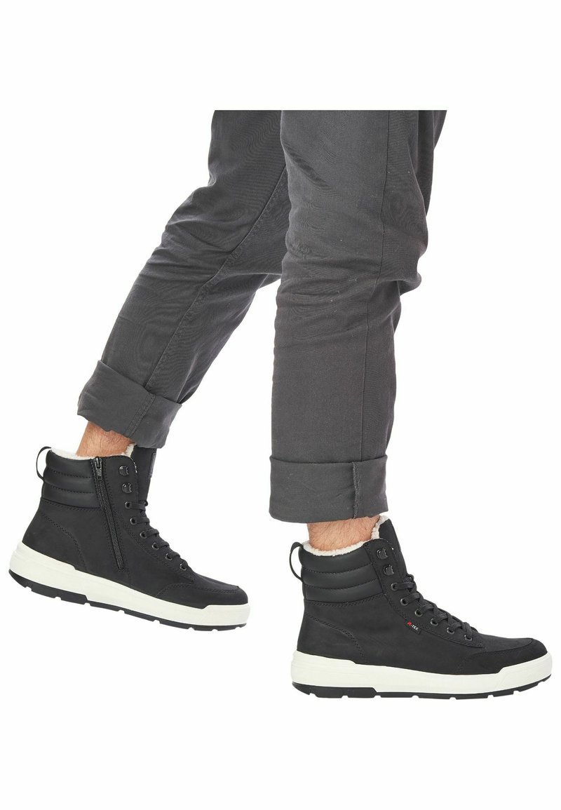 Bottines montantes noires en tissu texturé, avec semelles en caoutchouc blanc, fermeture éclair et col rembourré pour plus de confort.