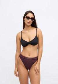 Zwarte bikinitop met dunne bandjes, gecombineerd met paarse, gestreepte bikinibroekjes met hoge taille en een decoratieve gouden gesp.