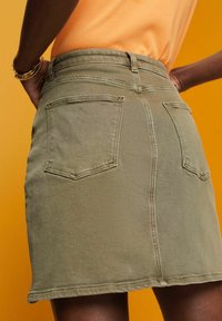 Olivgrüner Jeansrock mit tailliertem Bund, zwei Gesäßtaschen und geradem Schnitt. Der Stoff wirkt glatt mit sichtbaren Nähdetails.
