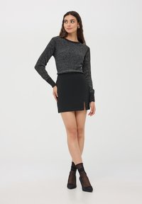 Maglione nero scintillante a maniche lunghe abbinato a una minigonna nera aderente con spacco laterale, completato da calze nere trasparenti e tacchi.