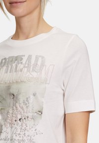T-shirt bianca in cotone con stampa grafica a design floreale argento e pastello, maniche corte e scollatura a girocollo.