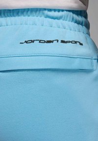 Jasnoniebieskie sportowe spodnie z teksturowanej tkaniny, z czarnym logo "Jordan Sport" na pasku w talii oraz elastycznym ściągaczem u góry.