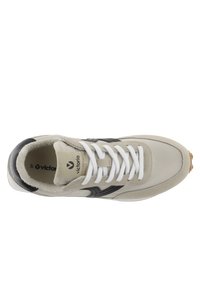 Sneaker grigio chiaro con tomaia in pelle, dettagli neri, lacci bianchi piatti e suola testurizzata. Fodera morbida visibile nel colletto.