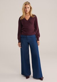Pull-over bordeaux avec texture côtelée et manches longues, associé à un jean bleu foncé taille haute à jambes larges et des escarpins à bout pointu.